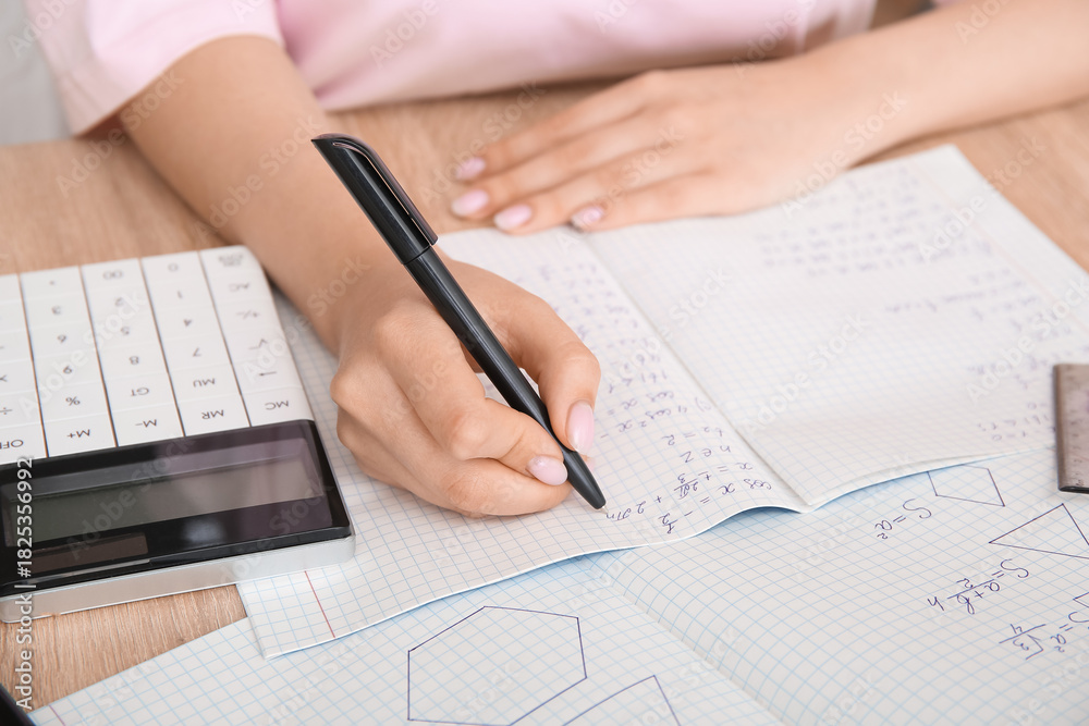 Naklejka premium Woman writing math formulas in copybook on wooden table