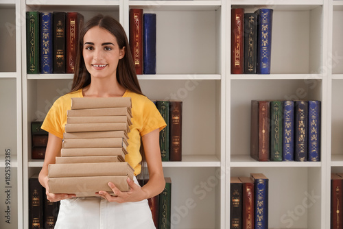 Happy female student with books near shelving unit in library