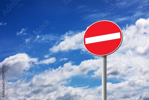 A universal 'No Entry' road sign (Prohibitory Sign) set against a bright blue, cloudy sky. Symbolizes restriction, danger, and boundaries, offering ample copy space for text.