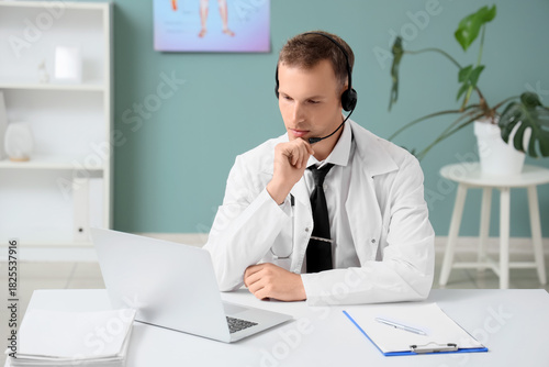 Thoughtful male doctor wearing a headset and white coat, providing online med...