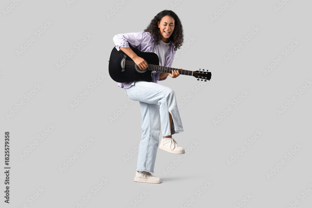 Obraz premium Happy young African-American woman playing acoustic guitar on white background