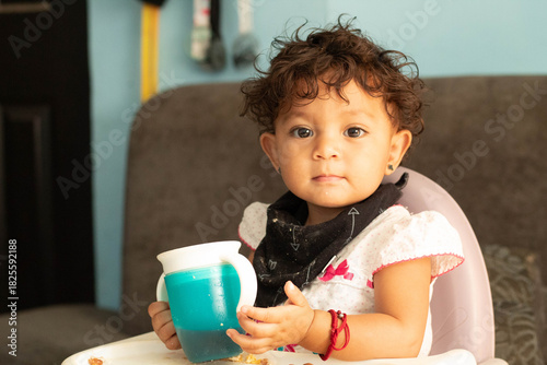 Cute toddler girl looking sideways holding drinking cup