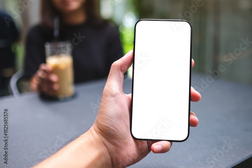 Mockup image of a man holding mobile phone with blank screen  with a blurred woman in background