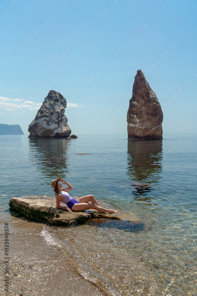 Fototapeta premium Woman, Swimsuit, Ocean. Young woman relaxing on a rock at the beach with majestic sea stacks.