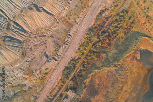 Aerial abstract composition showing industrial damage. Eroded quarry walls contrast with a geometric road and autumnal vegetation, illustrating technogenic pollution and land degradation.