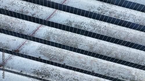 Rows of solar panels in an icy winter field. Aerial drone video slowly flying over a solar farm in winter for top down birds eye view of the solar array.