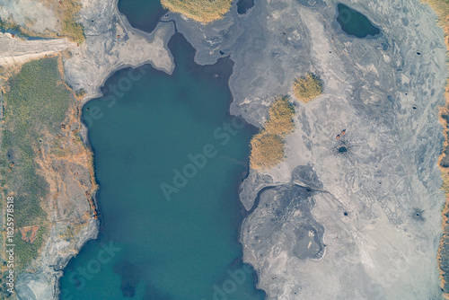 Aerial abstract of a mining tailings pond. The deep turquoise water contrasts sharply with the grey sludge, illustrating severe industrial pollution and environmental disaster.