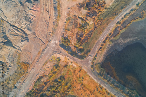 Aerial abstract composition of an industrial wasteland. Complex geometric road patterns intersect with eroded quarry textures and polluted water, illustrating severe land degradation.