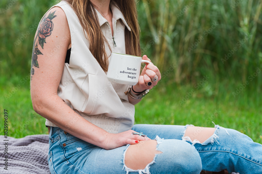 Obraz premium Woman holding coffee mug with tattoo and ripped jeans