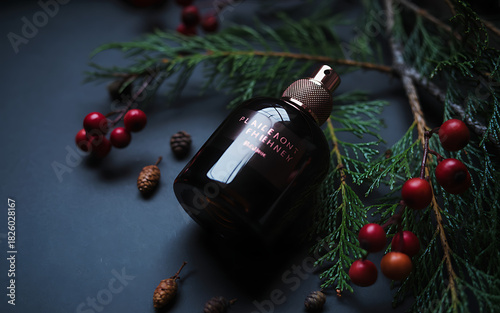 A dark glass perfume bottle with a gold cap rests among pine needles and berries