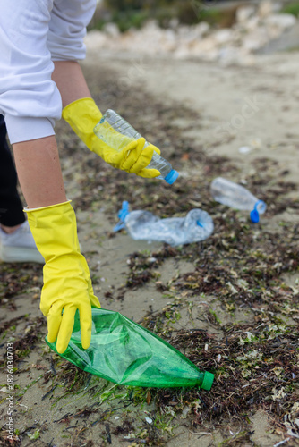 volunteer collecting plastic bottles on a polluted beach, highlighting ocean pollution, waste problem, environmental protection and coastal cleanup action.