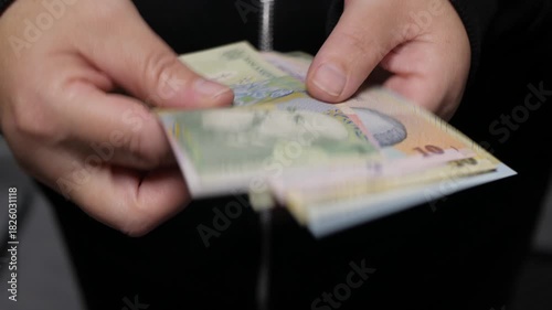 A close-up shot of hands carefully counting and fanning out Romanian Leu banknotes. The scene represents finance, banking, saving, payment, and currency exchange.