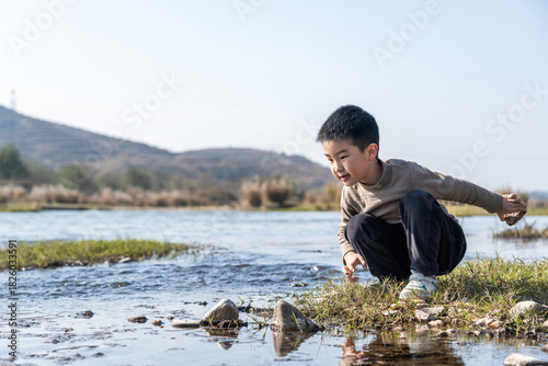 A young boy is crouching by the river, exploring the water in a natural outdoor environment.