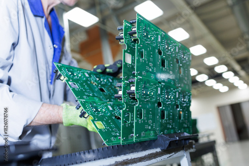 Worker handling assembled green circuit board panels at electronics factory