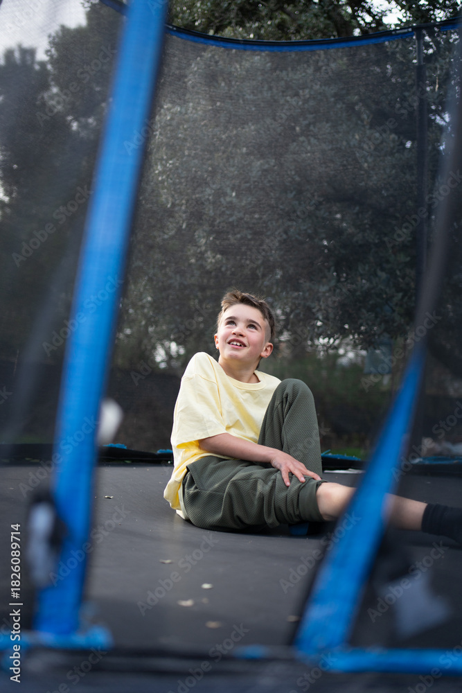 Obraz premium Smiling child sitting and relaxing on a trampoline after jumping