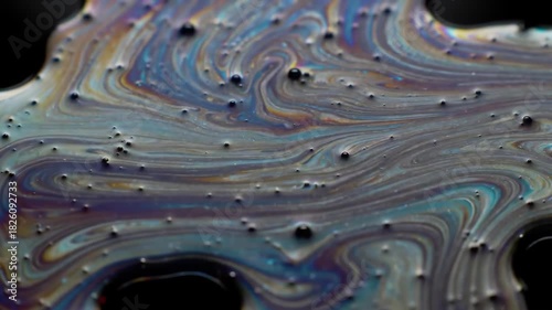 Close-up of colorful liquid paint swirling on a dark surface with bubbles