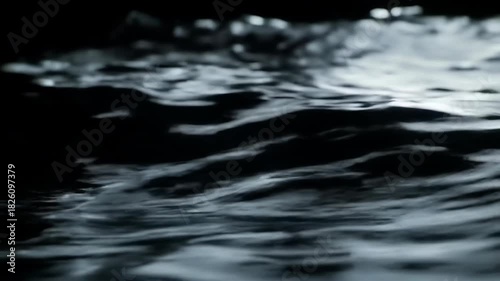 Calm water surface reflecting light in a dark environment, serene mood