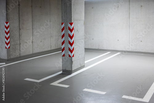 Empty indoor parking space with concrete walls, floor markings, and safety striped warnings on pillars.
