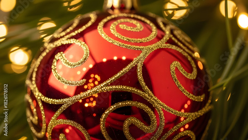 Red ornamental ball with golden pattern hanging on pine tree with blurry bokeh lights