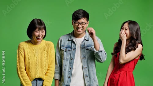 Three young Asian friends laughing together on a green screen background.