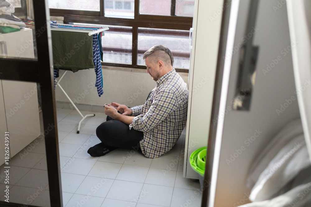 Fototapeta premium Man sitting on floor using smartphone feeling relaxed