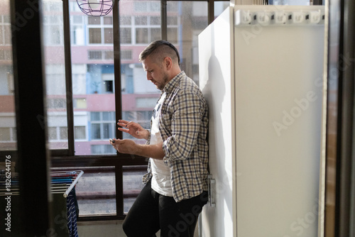 Young man using mobile phone leaning on wall