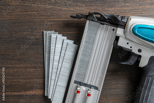 The part hammer of a power nail gun with of strips of finishing nails on wooden background. Pneumatic nail gun with metal brads, closeup, top view