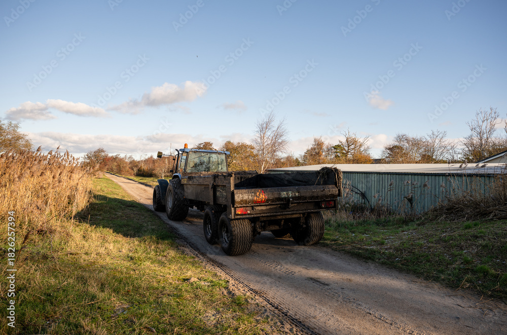 Obraz premium tractor with trailer driving on rural dirt road in autumn countryside