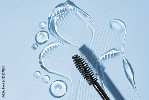 Close-up of transparent eyelash or eyebrow gel serum with black brush, smooth and shiny texture on blue background
