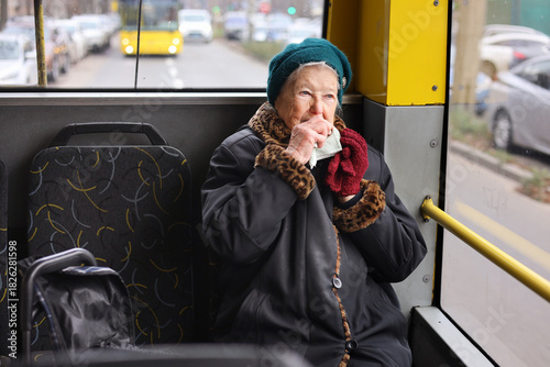 A senior woman is sitting on a bus, using her smartphone. She is traveling through the city, enjoying her journey in a relaxed manner.