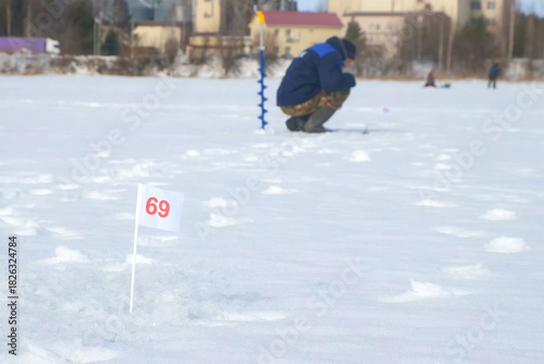 Fisherman waiting for fish biting on frozen lake on catching fish competition. Man catches fish on frozen river with ice and snow. Outdoor winter activity hobby leisure recreation kind of sport.