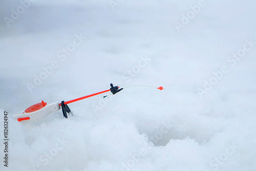 Red fishing float on rod bobbing near ice fishing hole during winter fishing. Outdoor winter activity hobby leisure recreation kind of sport. Competition in catching fish.