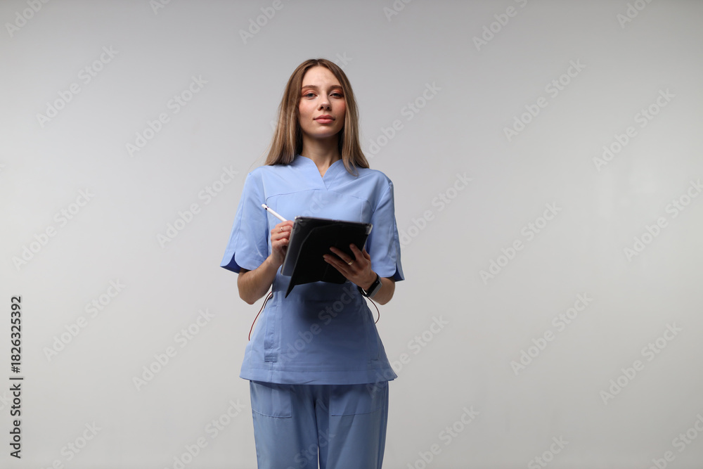 Fototapeta premium Young caucasian female nurse in blue scrubs holding digital tablet