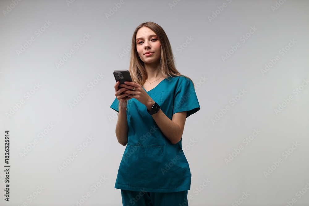 Naklejka premium Young caucasian female nurse using smartphone in scrubs against white background