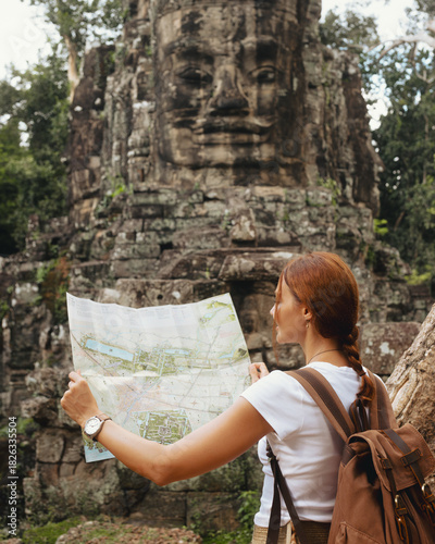 Fotografija Bayon Face Tower Angkor Thom With Female Traveler Reading Map, Cambodia