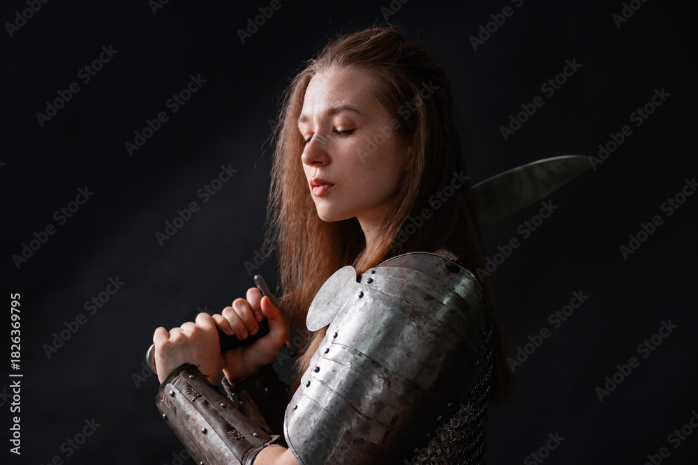 Naklejka premium Portrait of a young woman, fantasy warrior in armor with a sword in her hands isolated on a dark background.