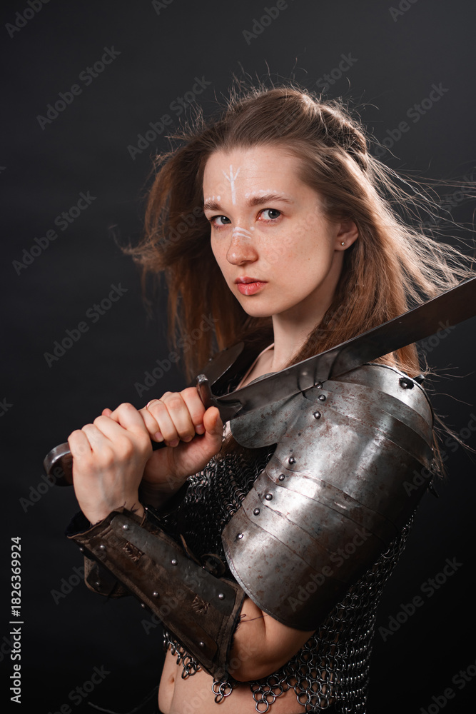 Obraz premium Portrait of a young woman, fantasy warrior in armor with a sword in her hands isolated on a dark background.