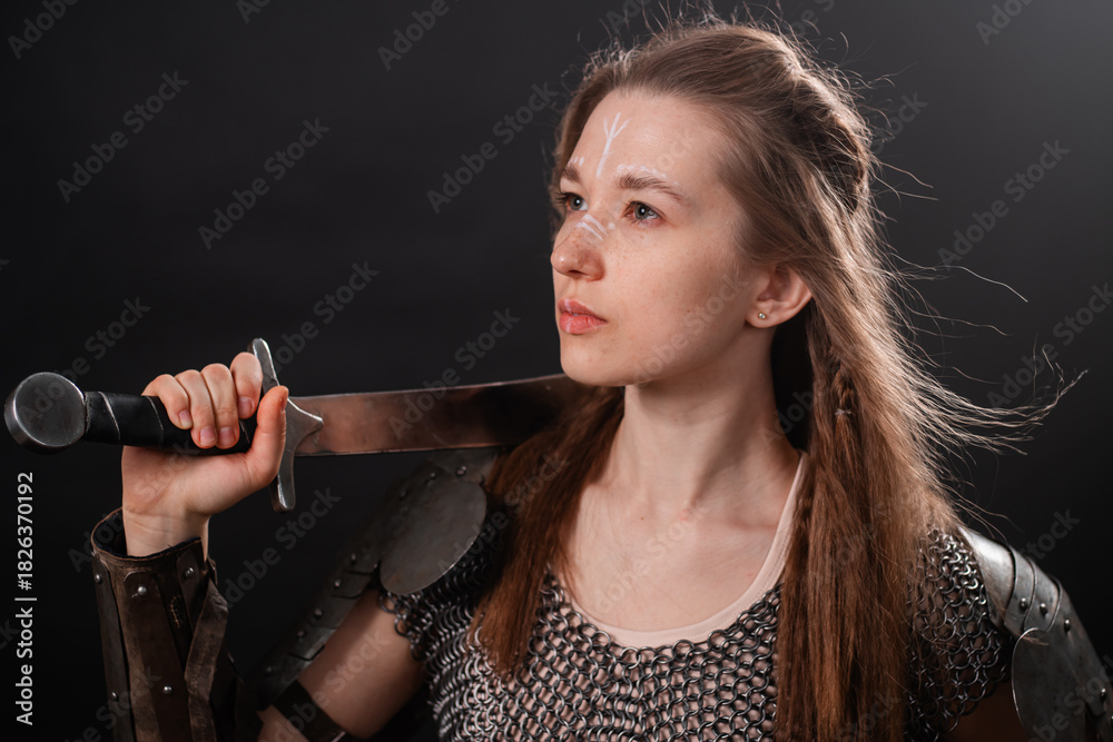 Obraz premium Portrait of a young woman, fantasy warrior in armor with a sword in her hands isolated on a dark background.