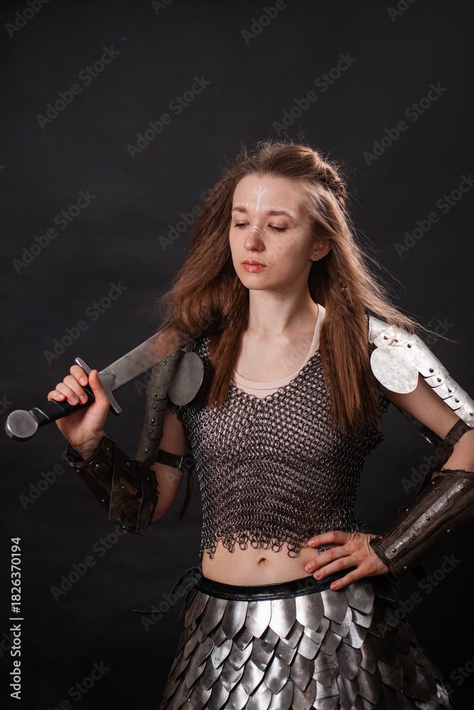 Obraz premium Portrait of a young woman, fantasy warrior in armor with a sword in her hands isolated on a dark background.