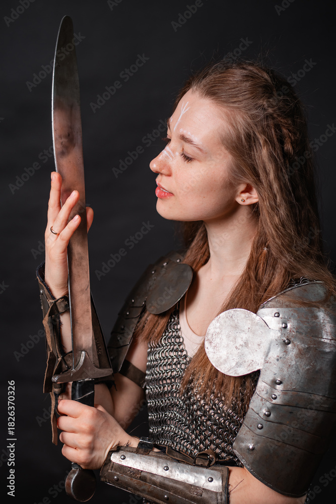 Obraz premium Portrait of a young woman, fantasy warrior in armor with a sword in her hands isolated on a dark background.