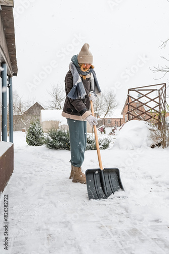 Woman shoveling snow on a home walkway during light snowfall winter safety and snow removal  warm clothing  shovelresidential outdoor scene