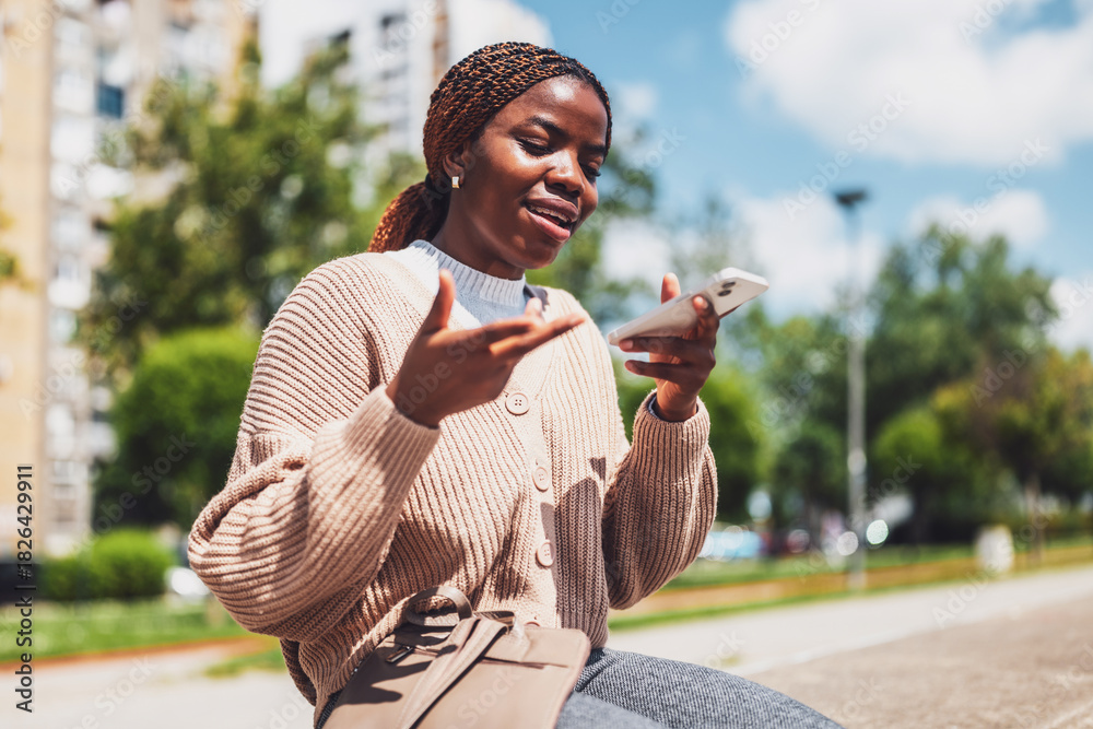 Fototapeta premium Young black woman is using smartphone. She is recording voice message.