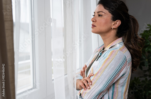Free Download Young woman in a blue shirt gently touching a sheer curtain and gazing outside, enjoying calm morning light with a peaceful thoughtful expression, a mindful pause at home, optimism and quiet self care - GFXLoad