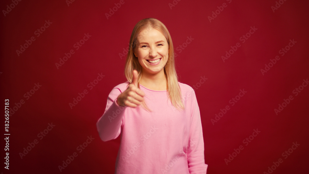 Fototapeta premium Smiling cheerful blonde woman nodding yes with head showing thumb up isolated on red background