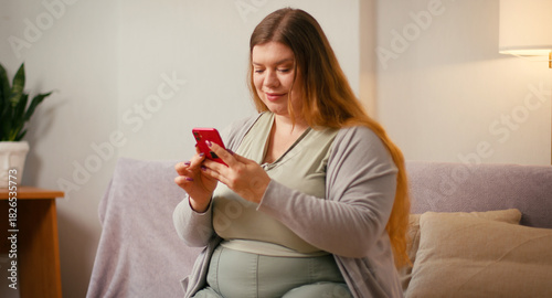 Plus size woman scrolls smartphone while sitting on couch