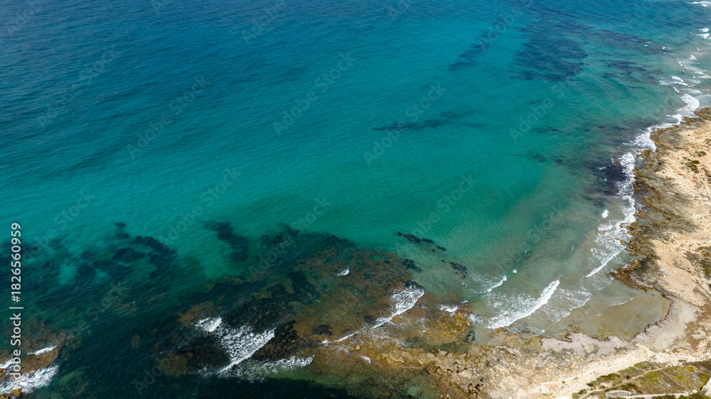 Fototapeta premium Aerial view of the rocky coastline overlooking the sea. The water ranges from turquoise to blue and is very clean and transparent. Located in Sicily, Italy. Sunny summer day.