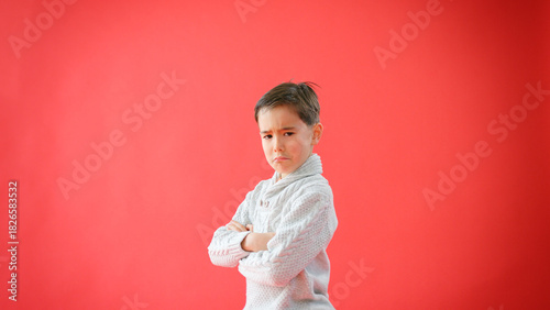 Portrait Of Serious Young Boy With Folded Arms Against Red Studio Background