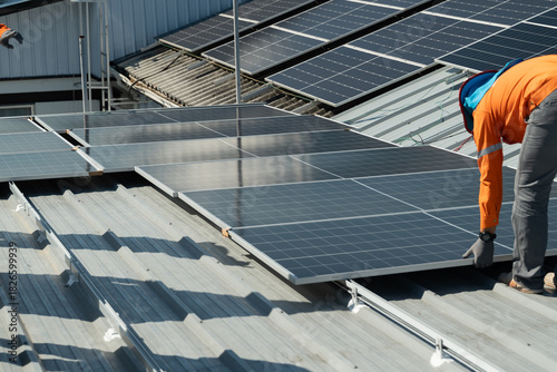 Workers install solar panels on a metal roof during bright daytime in a green energy project