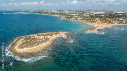 Aerial view of Isola delle Correnti, a small rocky island near the coast. In background is the Sicilian coastline, located near Portopalo in the province of Syracuse, Sicily, Italy. Sunny summer day.