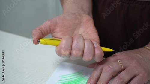 A person using a yellow pen to practice hand exercises to improve grip strength.